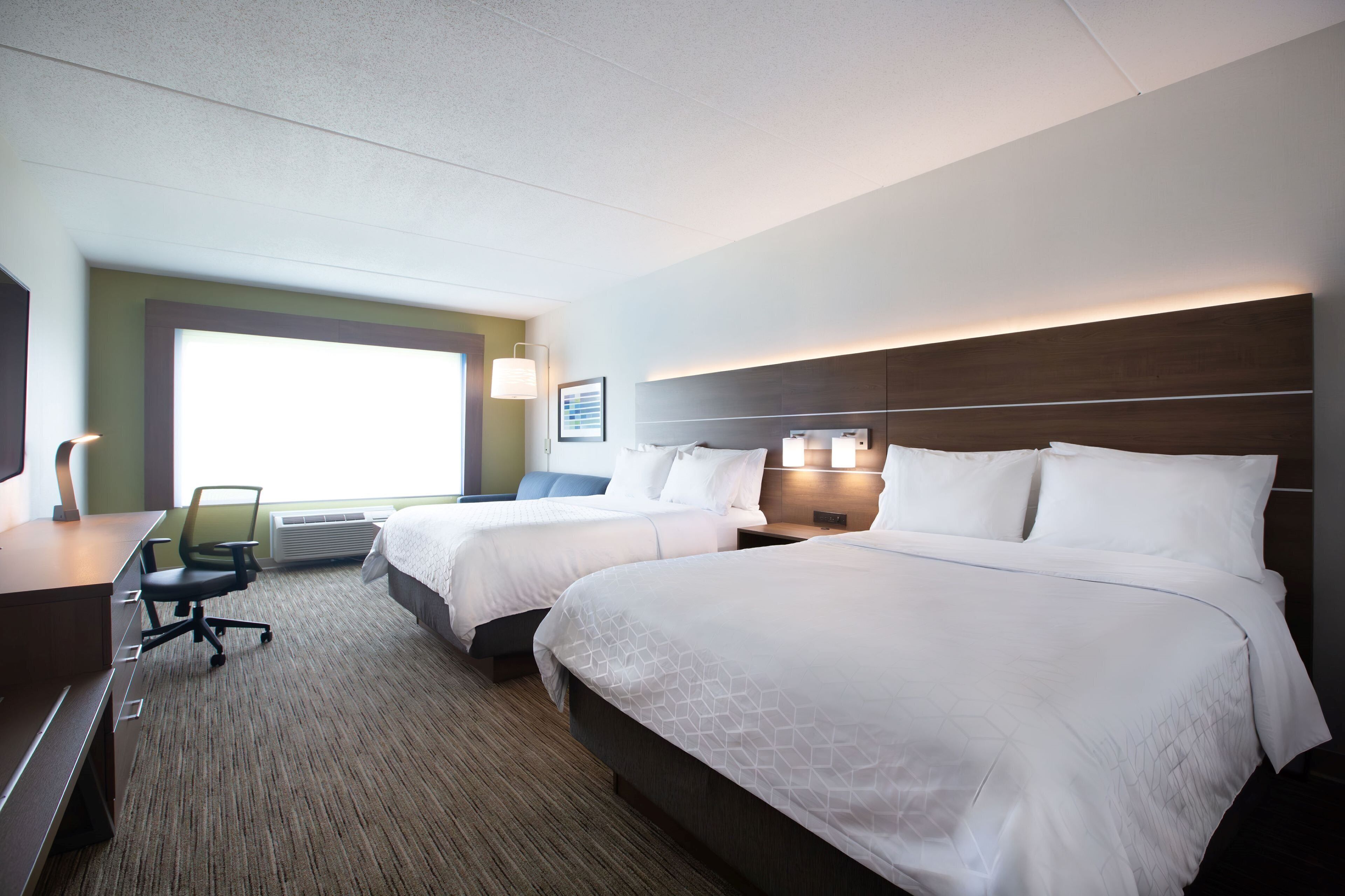 A hotel room with two beds, a desk, and a chair.