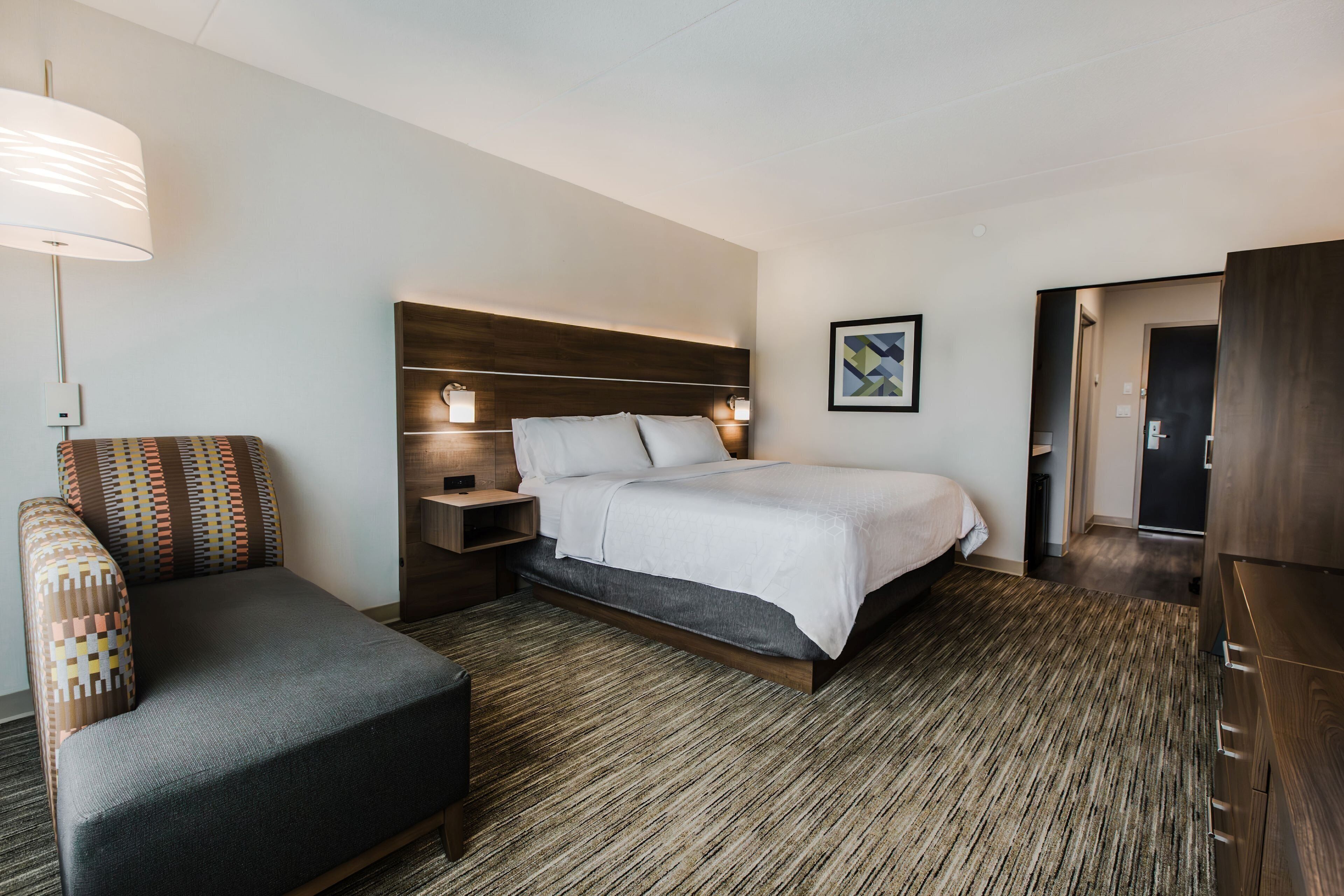 Una habitación de hotel moderna con una cama grande, un sofá, una mesita de noche y una lámpara.