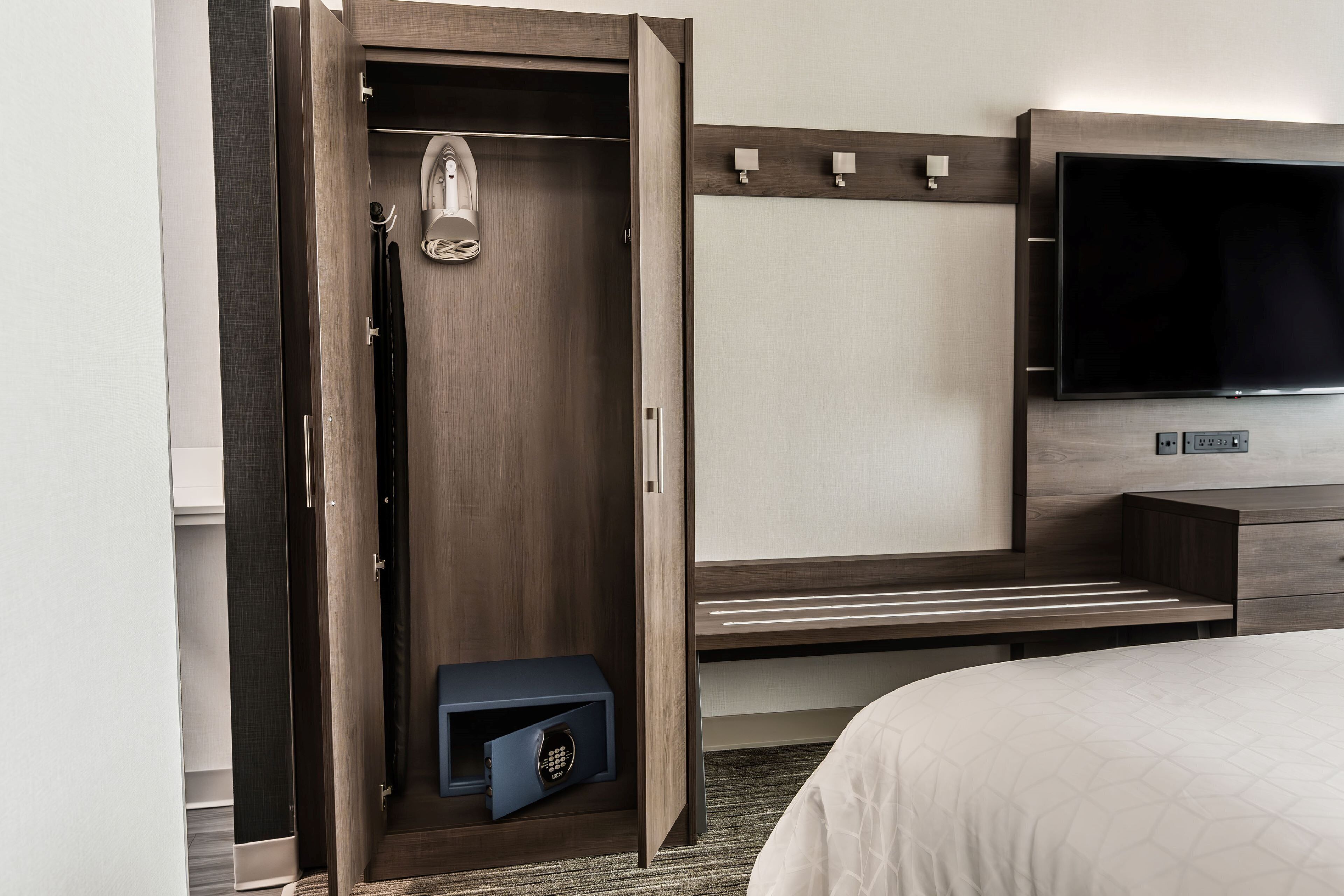 A hotel room with a wooden wardrobe, a television mounted on the wall, and a small safe.