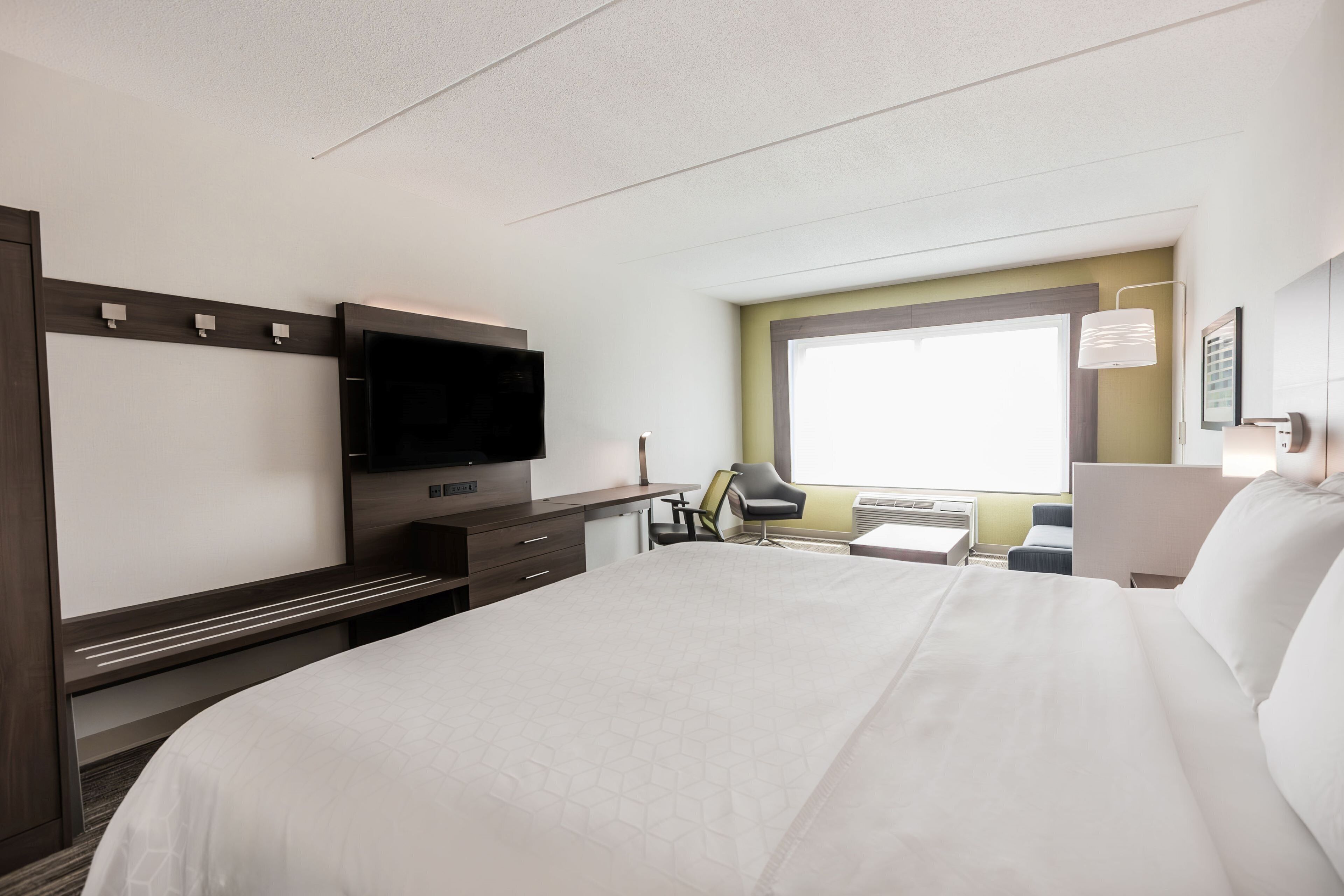 Quarto de hotel com uma cama grande, uma escrivaninha com cadeira, televisão de tela plana e janela com vista.