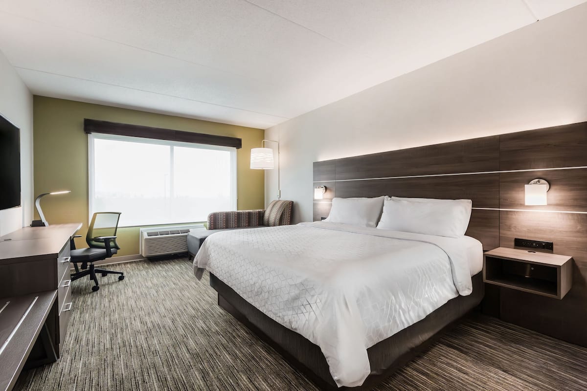 A hotel room with a large bed, a desk, a chair, and a TV.
