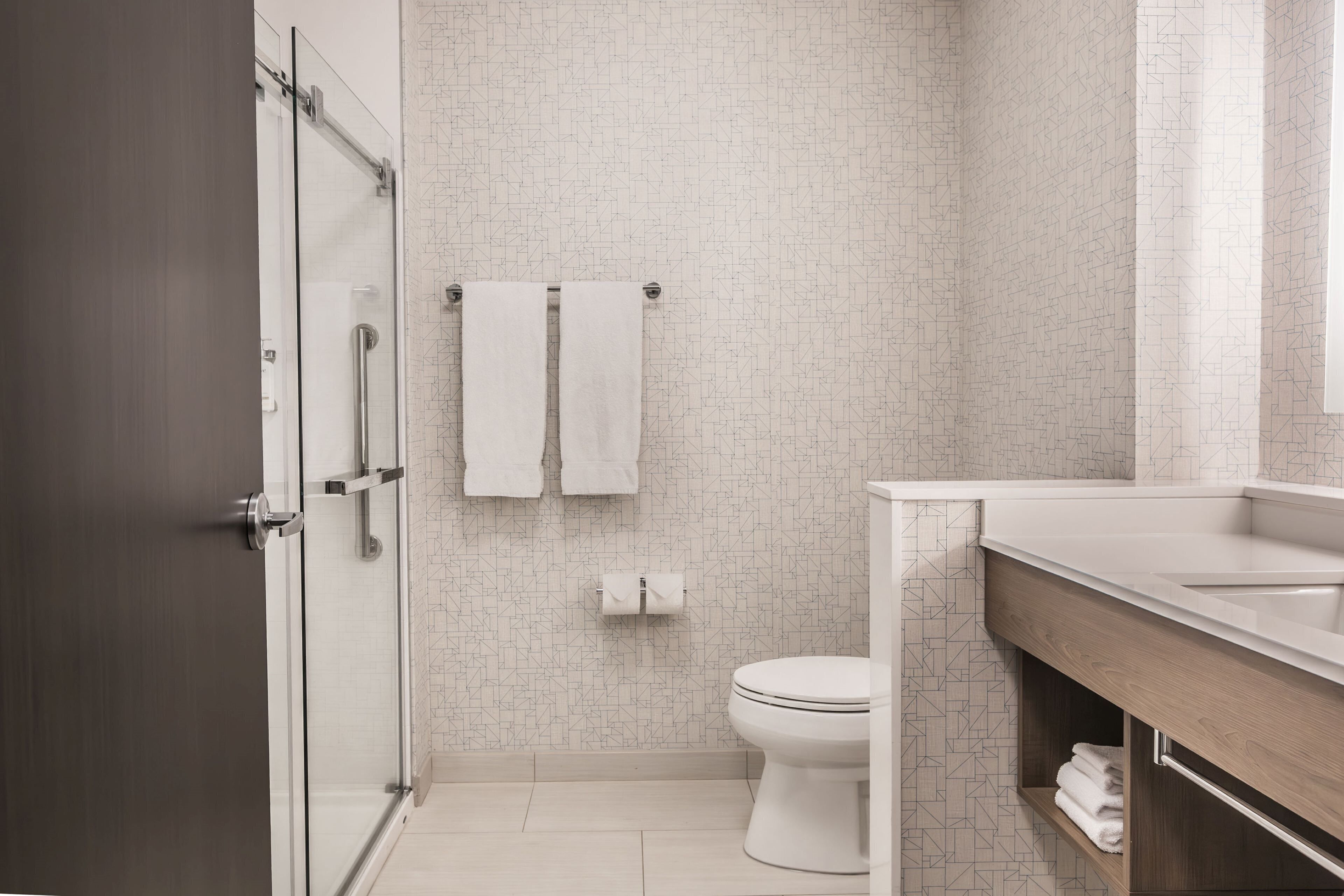 Un baño moderno con cabina de ducha de vidrio, inodoro y tocador con lavamanos.