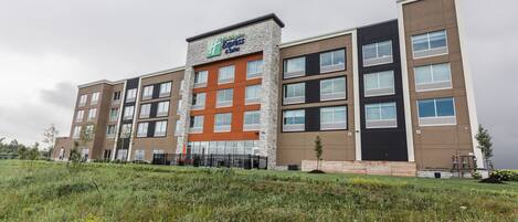 A multi-story hotel with a prominent 'Hilton Express' sign, featuring a modern design with a mix of stone and brick facades, large windows, and a flat roof.