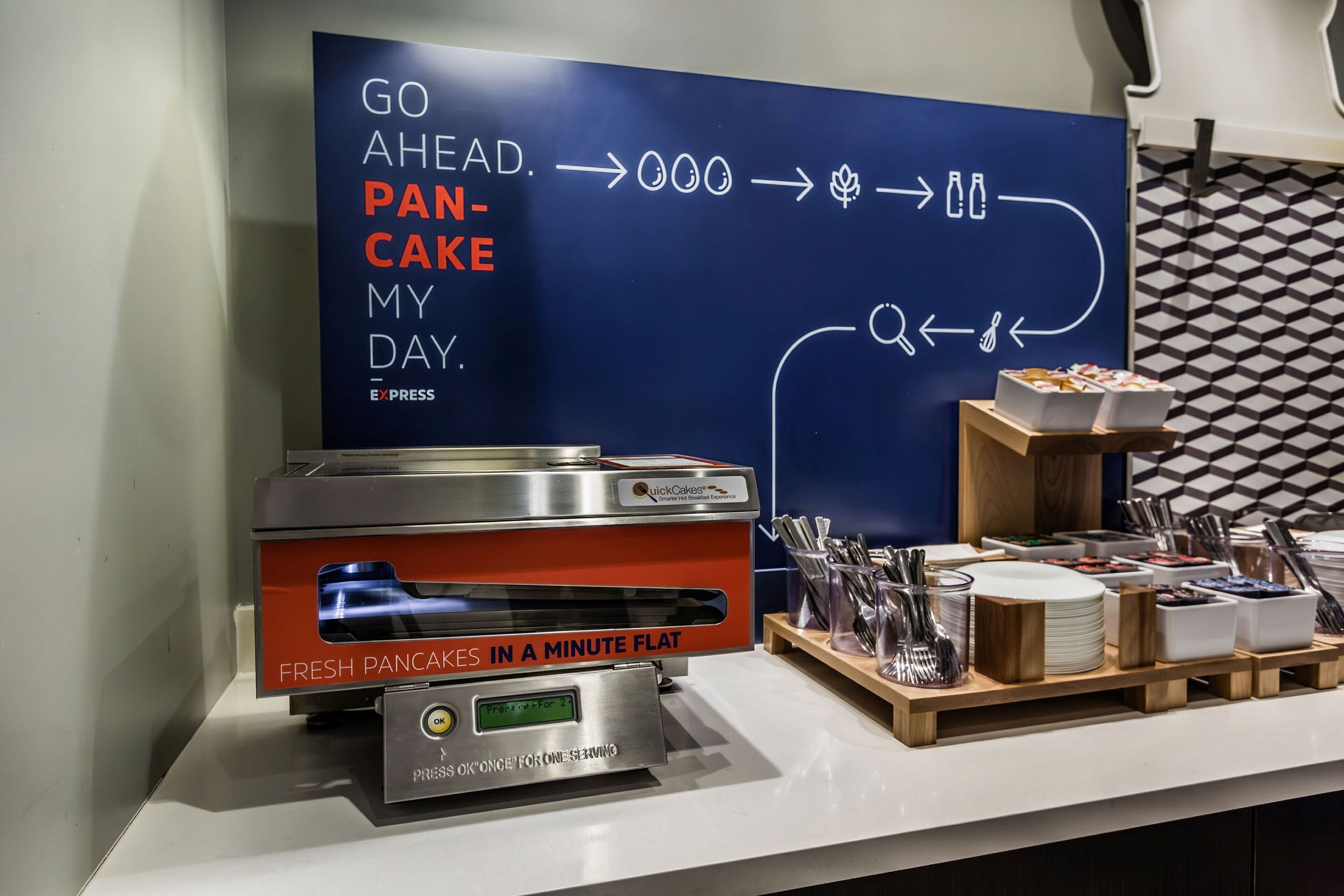 Una estación de desayuno con una máquina QuickCake Express, utensilios y un cartel que promociona el servicio.