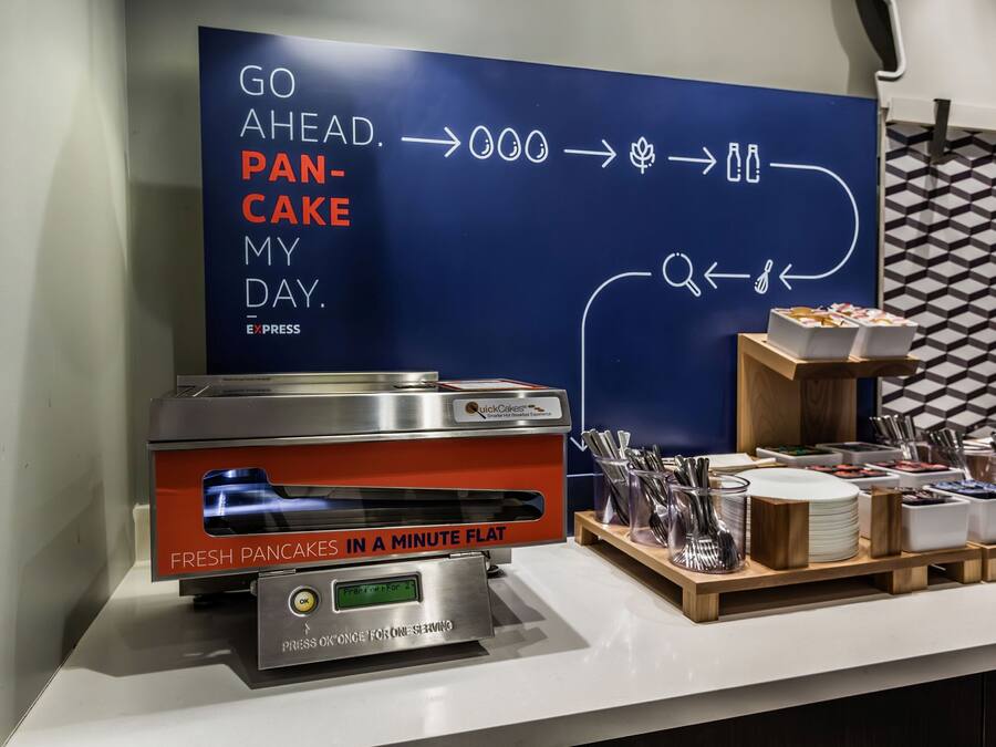 A breakfast station with a QuickCake Express machine, utensils, and a sign promoting the service.