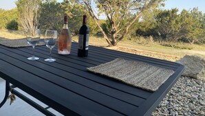 A table with a bottle of wine and two glasses on a wooden deck with a view of trees and a clear sky.