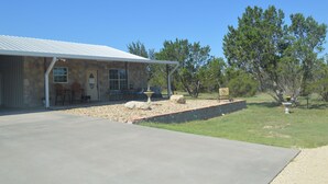A stone building with a covered patio, outdoor seating, and a landscaped yard with trees.