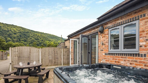 A hot tub in a backyard with a wooden table and benches, a brick house, and a wooden fence. - 3 bedroom accommodation in Trevor, near Llangollen (Trevor, near Llangollen)
