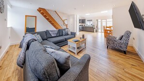 A modern living room with a sofa, coffee table, and patterned armchair. A wooden staircase leads to a balcony. - 3 bedroom accommodation in Trevor, near Llangollen (Trevor, near Llangollen)