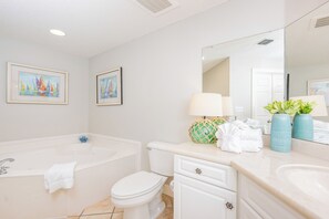 A bathroom with a bathtub, toilet, vanity with a mirror, and two framed paintings on the wall. - Phoenix On The Bay 1521 Bay View (Orange Beach)