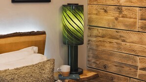 Uma cama com edredom branco, cabeceira de madeira, um vaso verde, uma xícara de café e uma prateleira de madeira com livros.