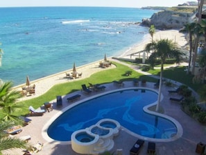 Un'area piscina con design curvo, circondata da poltrone prendisole e palme, con vista su una spiaggia e l'oceano.