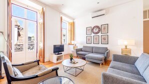 Ein modernes Wohnzimmer mit Sofa, Sesseln, Couchtisch, Fernseher und gerahmten Kunstwerken an der Wand.