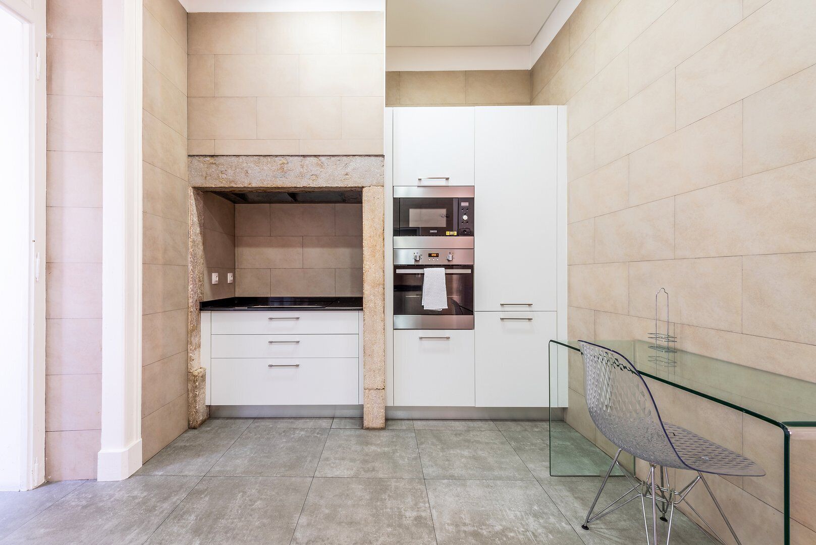 Una cocina compacta con horno integrado, microondas y una mesa de comedor de vidrio.