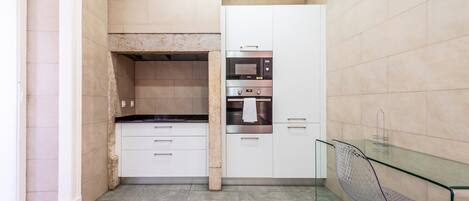 Una cocina compacta con horno integrado, microondas y una mesa de comedor de vidrio.