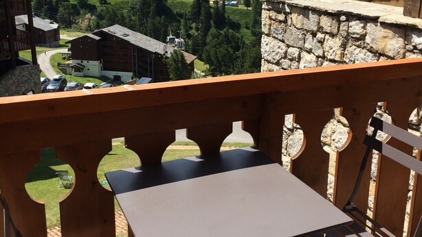 A balcony with a table and chairs overlooking a mountainous landscape with buildings and a road. - BELLE PLAGNE 2 rooms, sleeps 5-6, ski-in/ski-out + covered parking included (LA PLAGNE)