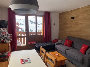 Une pièce chaleureuse avec un canapé, une table et une vue sur un paysage enneigé, visible à travers de grandes fenêtres.