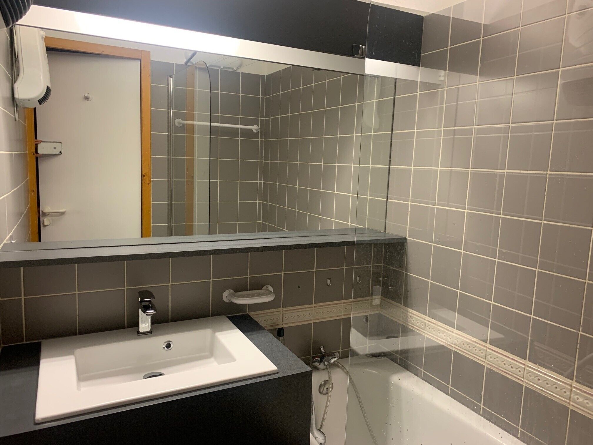 Un baño con un lavamanos blanco, cabina de ducha de vidrio y un espejo grande.