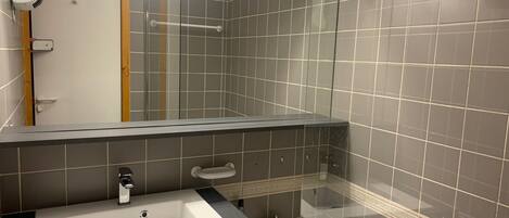 Un baño con un lavamanos blanco, cabina de ducha de vidrio y un espejo grande.