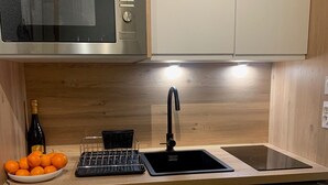 A compact kitchen with a microwave, sink, and dishwasher. There is a bowl of oranges and a bottle of wine on the counter. - BELLE PLAGNE 2 rooms, sleeps 5-6, ski-in/ski-out + covered parking included (LA PLAGNE)