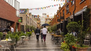 Een voetgangersstraat met terrasjes en plantenbakken, waar mensen lopen en dineren.