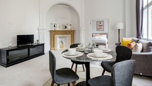 Una sala de estar moderna con una mesa de comedor para cuatro personas, una chimenea, un televisor sobre un mueble negro y un sofá gris con cojines amarillos.