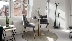 Een moderne eetruimte met een ronde tafel, twee stoelen, een vaas met takken en een kapstok.