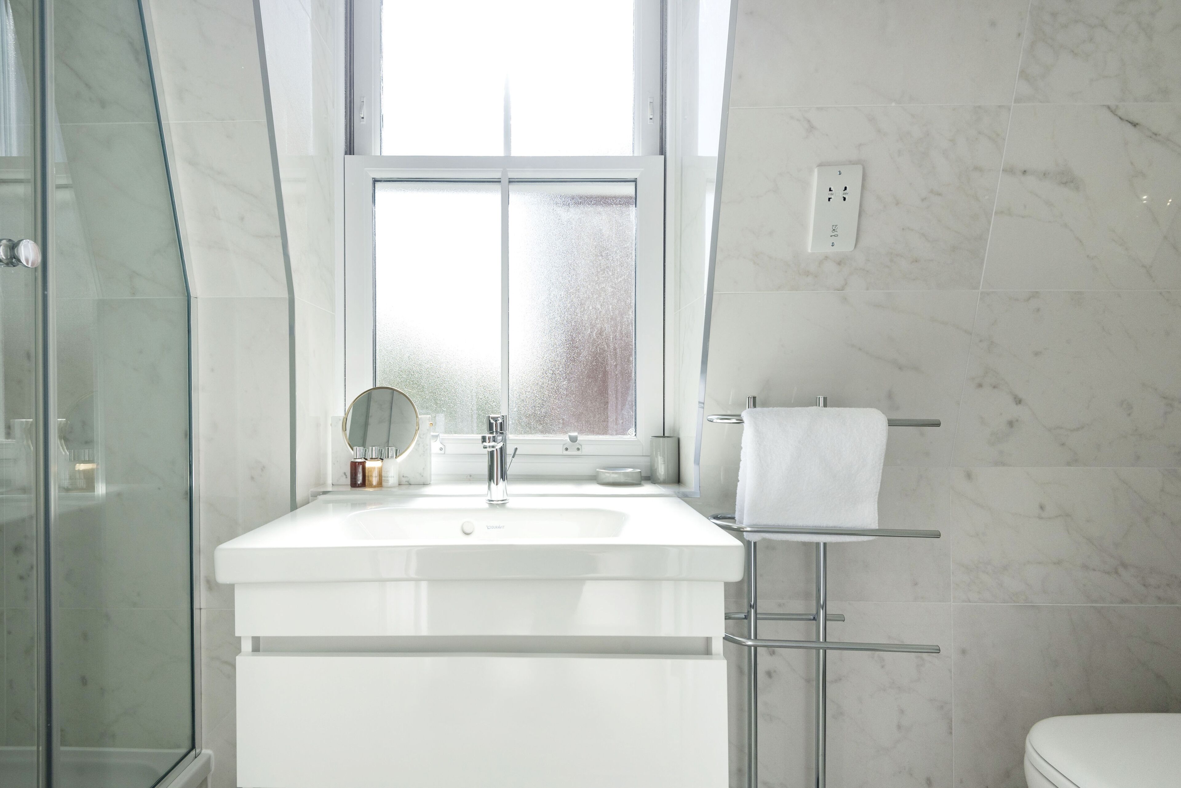 Een moderne badkamer met een douchecabine van glas, een witte wastafel en een handdoekrek.