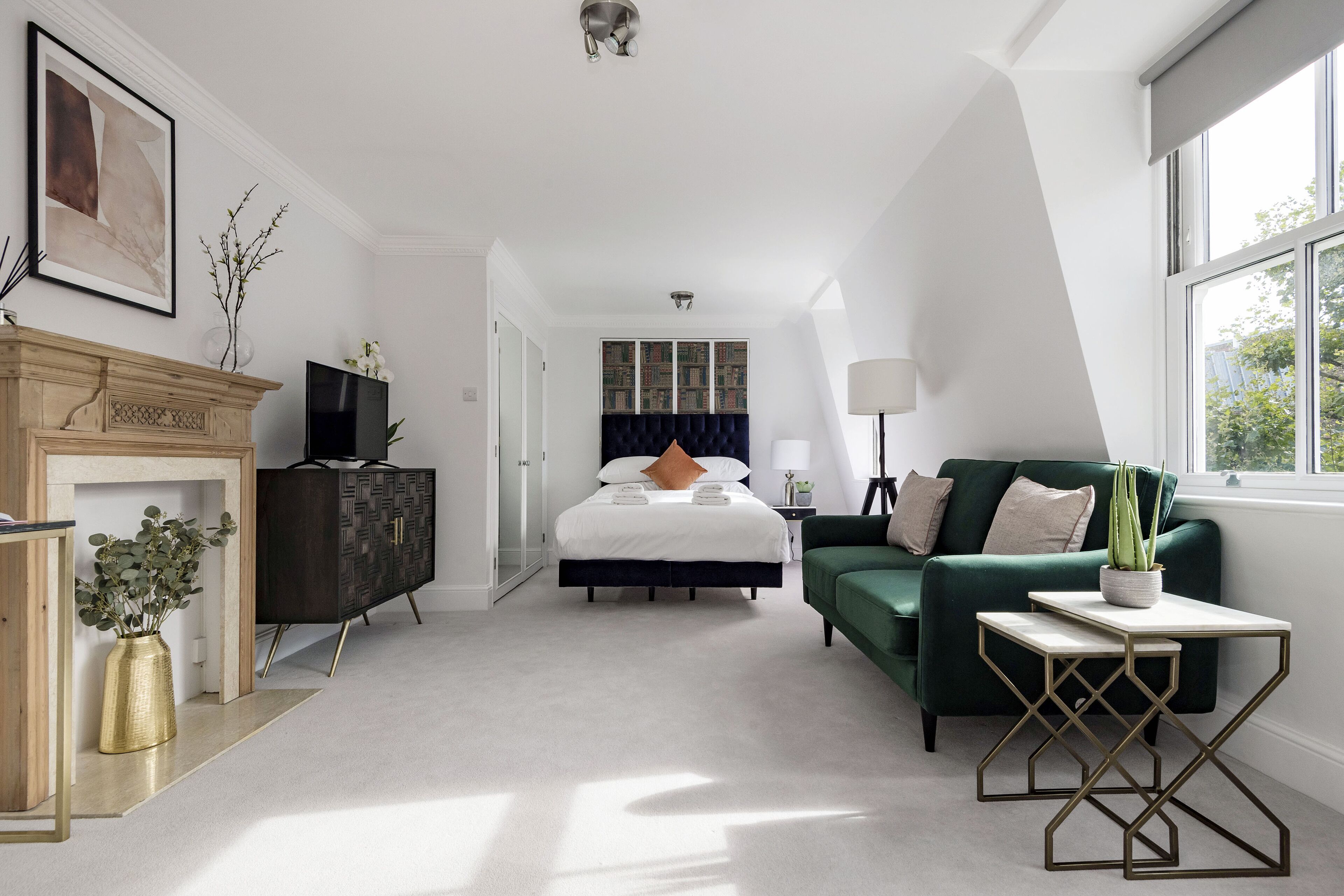 A modern hotel room with a bed, a green sofa, a small table, a TV, and a fireplace.