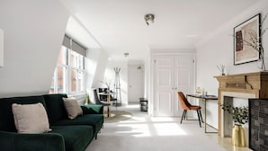 Een moderne woonkamer met een groene bank, een open haard en een eethoek met een tafel en stoelen.