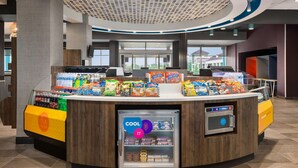 Un angolo self-service con bevande e snack assortiti, un banco frigo e un terminale per pagamenti digitali.
