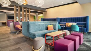 Un'area lounge moderna con un divano blu, pouf viola e rosa, un tavolino in legno e diverse poltrone colorate.