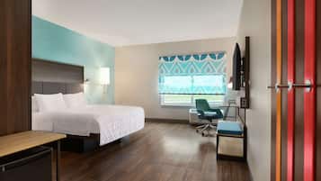 A hotel room with a bed, desk, chair, TV, and window with blinds.