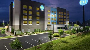 Un moderno edificio alberghiero con un evidente cartello 'tru by Hilton', un parcheggio e aree verdi curate.