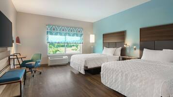 A hotel room with two beds, a desk, a chair, a TV, and a window with a view of greenery.