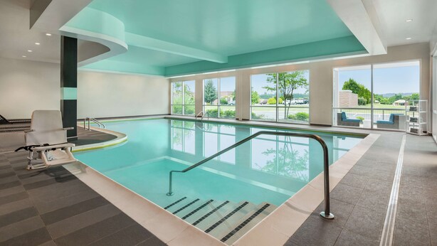 Una piscina interna moderna con pareti di vetro trasparenti, un'area salotto a bordo vasca e vista sull'esterno.