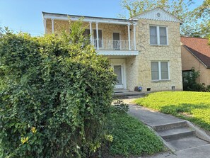 A two-story house with a stone facade, a balcony, and a well-maintained front yard.
