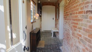 A hallway with a brick wall, a bench, and a door with a light fixture. - Picturesque cottage for two in the Kent countryside - Moat Farm Cottage (Ash)