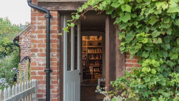 A brick building with a doorway leading to a room with bookshelves and a bench. - Picturesque cottage for two in the Kent countryside - Moat Farm Cottage (Ash)