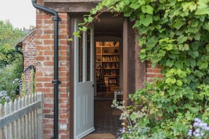 A brick building with a doorway leading to a room with bookshelves and a bench. - Picturesque cottage for two in the Kent countryside - Moat Farm Cottage (Ash)