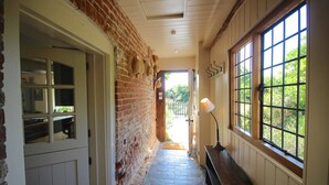 A narrow hallway with a brick wall, a wooden bench, and a large window with a view of greenery. - Picturesque cottage for two in the Kent countryside - Moat Farm Cottage (Ash)