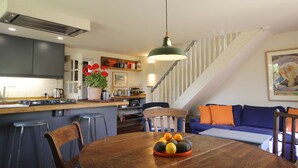 A modern kitchen with a central island, a dining table with fruit, and a staircase leading to a living area with a sofa. - Picturesque cottage for two in the Kent countryside - Moat Farm Cottage (Ash)