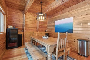 Cozy cabin interior with a dining table, hanging light, and large window offering a view of the outdoors.