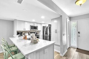 A modern kitchen with white cabinetry, a marble island, and stainless steel appliances.