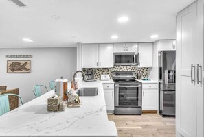 Une cuisine moderne avec des meubles blancs, un îlot central, des appareils en acier inoxydable et un revêtement mural décoratif.
