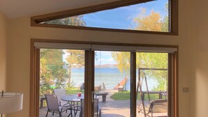 Ein Zimmer mit einer großen Schiebeglastür, die auf eine Terrasse mit Tisch und Stühlen führt, mit Blick auf ein Gewässer.