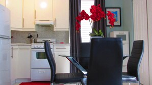 A compact kitchen with white cabinets, a stove, and a dining area with two black chairs and a glass table. - Beautiful Studio on Collins Ave by the Beach with Private Parking (Miami Beach)