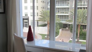 A modern room with a white desk and chair, large windows with a view of a building and palm trees. - Beautiful Studio on Collins Ave by the Beach with Private Parking (Miami Beach)