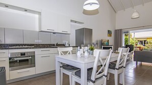 A modern kitchen with white cabinetry, a built-in oven, and a dining area with white chairs and a table. - Luxury Vacation Apartment "Casa Blou Curacao" Blije Rust 13 near Blue Bay Resort (Willemstad)