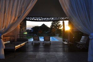 Un espace extérieur aménagé avec une piscine, un patio couvert et une vue sur la montagne au coucher du soleil.